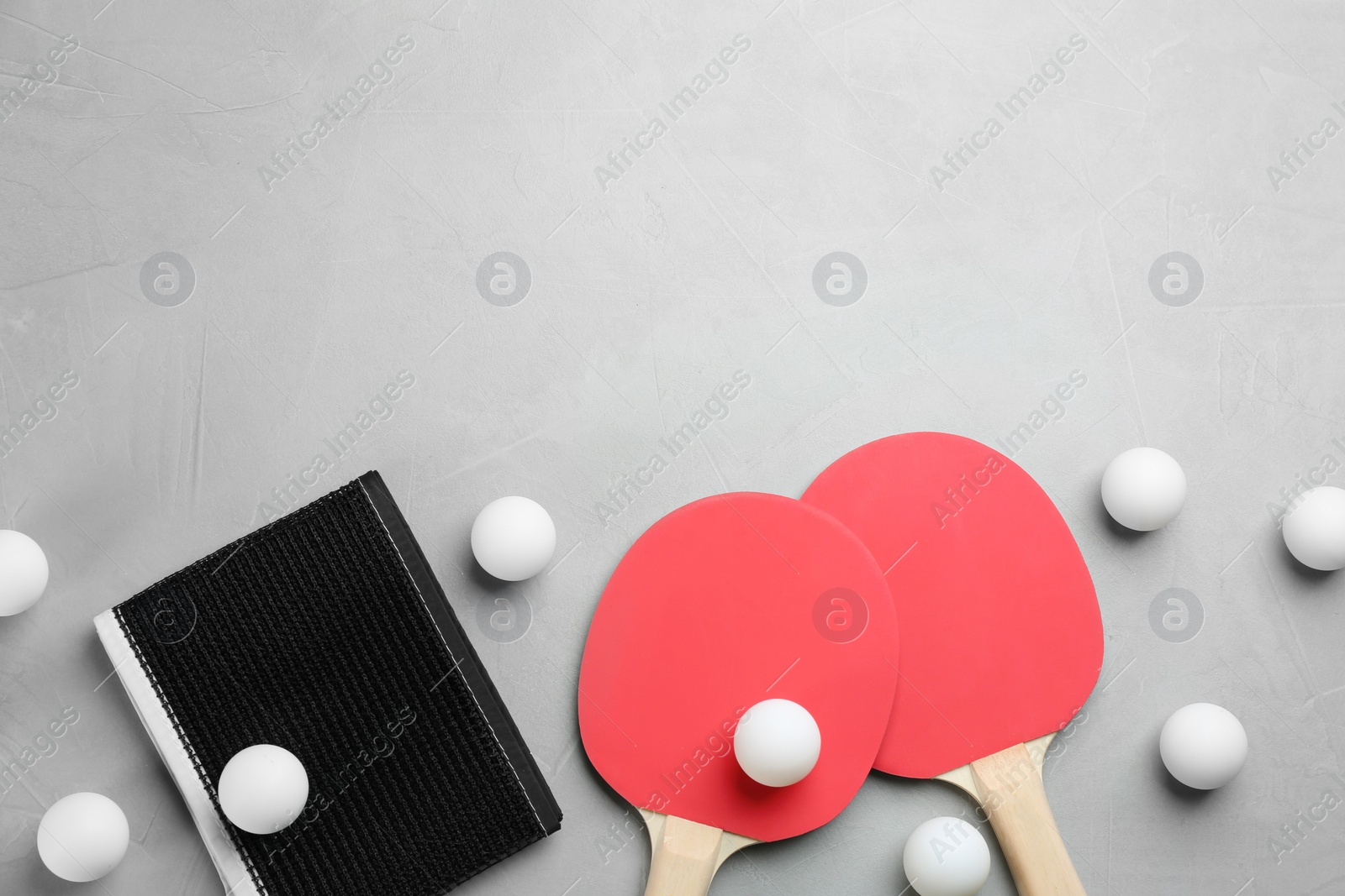 Photo of Ping pong rackets, net and balls on grey table, flat lay. Space for text