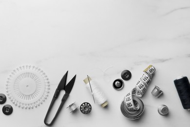 Photo of Threads and other sewing supplies on white marble table, flat lay. Space for text