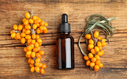 Photo of Natural sea buckthorn oil and fresh berries on wooden table, flat lay