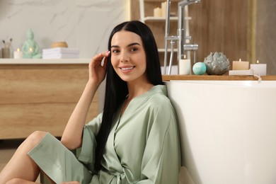 Photo of Beautiful young woman sitting near tub in bathroom