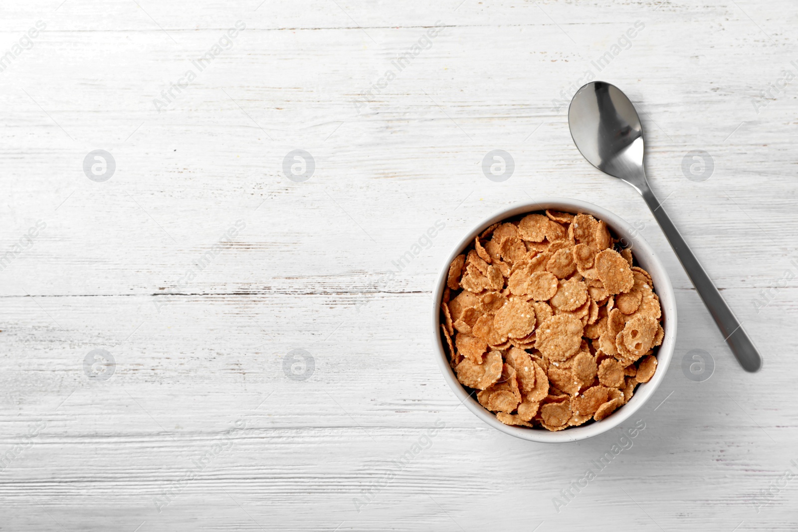 Photo of Bowl of cornflakes on light table, top view with space for text. Whole grain cereal for breakfast