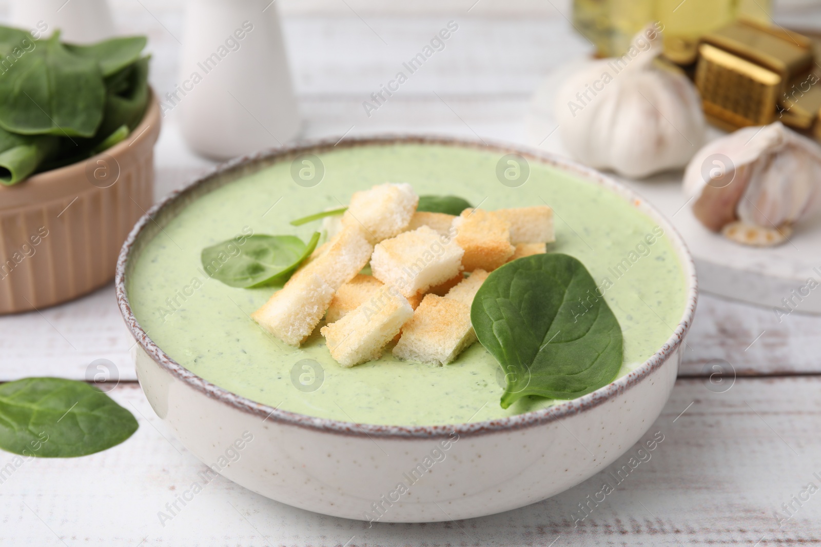 Photo of Delicious spinach cream soup with leaves and croutons in bowl on white wooden table