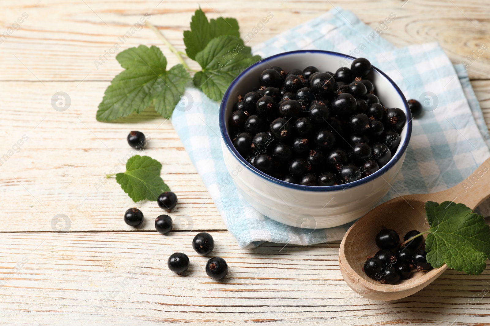 Photo of Ripe blackcurrants and leaves on light wooden table. Space for text