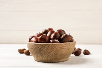 Fresh sweet edible chestnuts in bowl on white wooden table