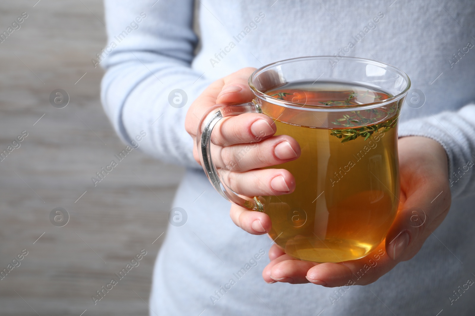 Photo of Woman holding cup of tasty herbal tea with thyme, closeup. Space for text