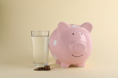 Water scarcity concept. Piggy bank, glass of drink and coins on beige background