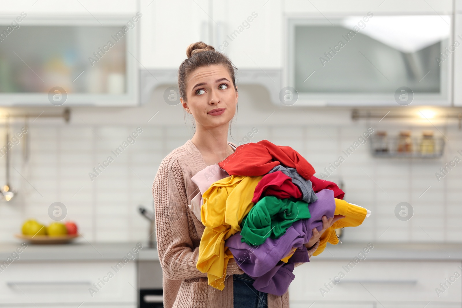 Photo of Woman holding pile of dirty laundry in kitchen