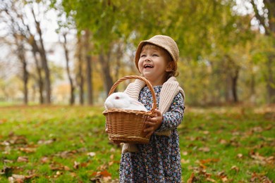 Happy girl holding basket with cute white rabbit in autumn park