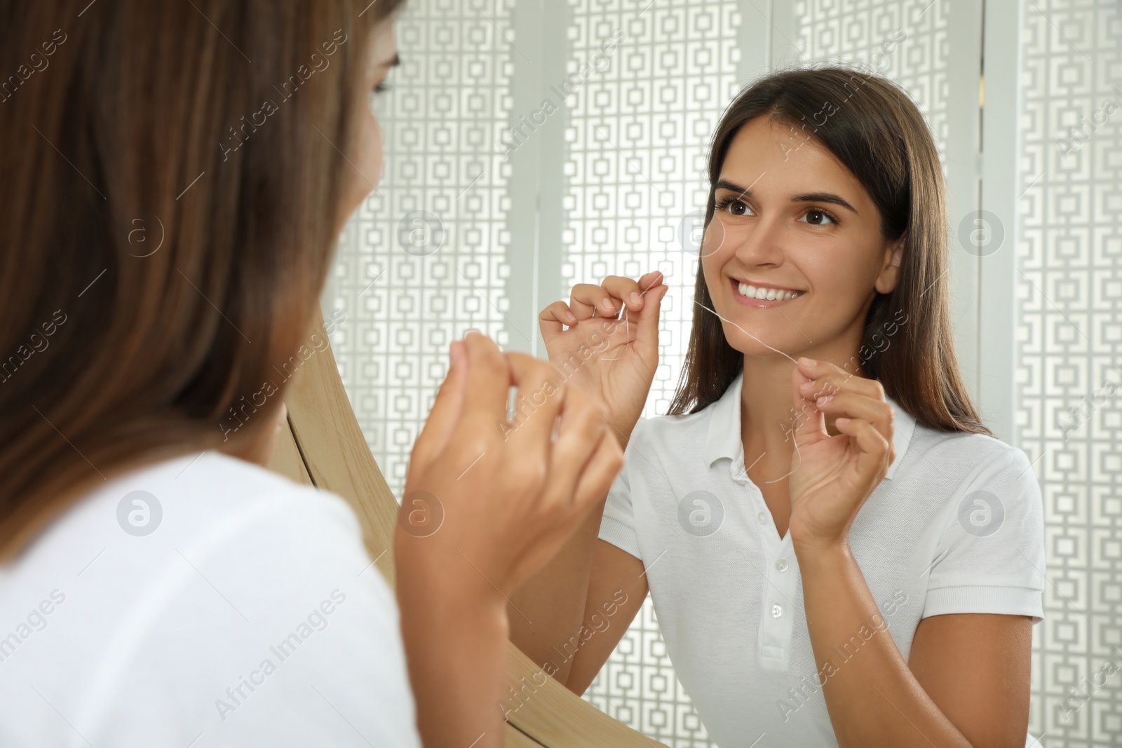 Photo of Young woman flossing her teeth near mirror at home. Cosmetic dentistry