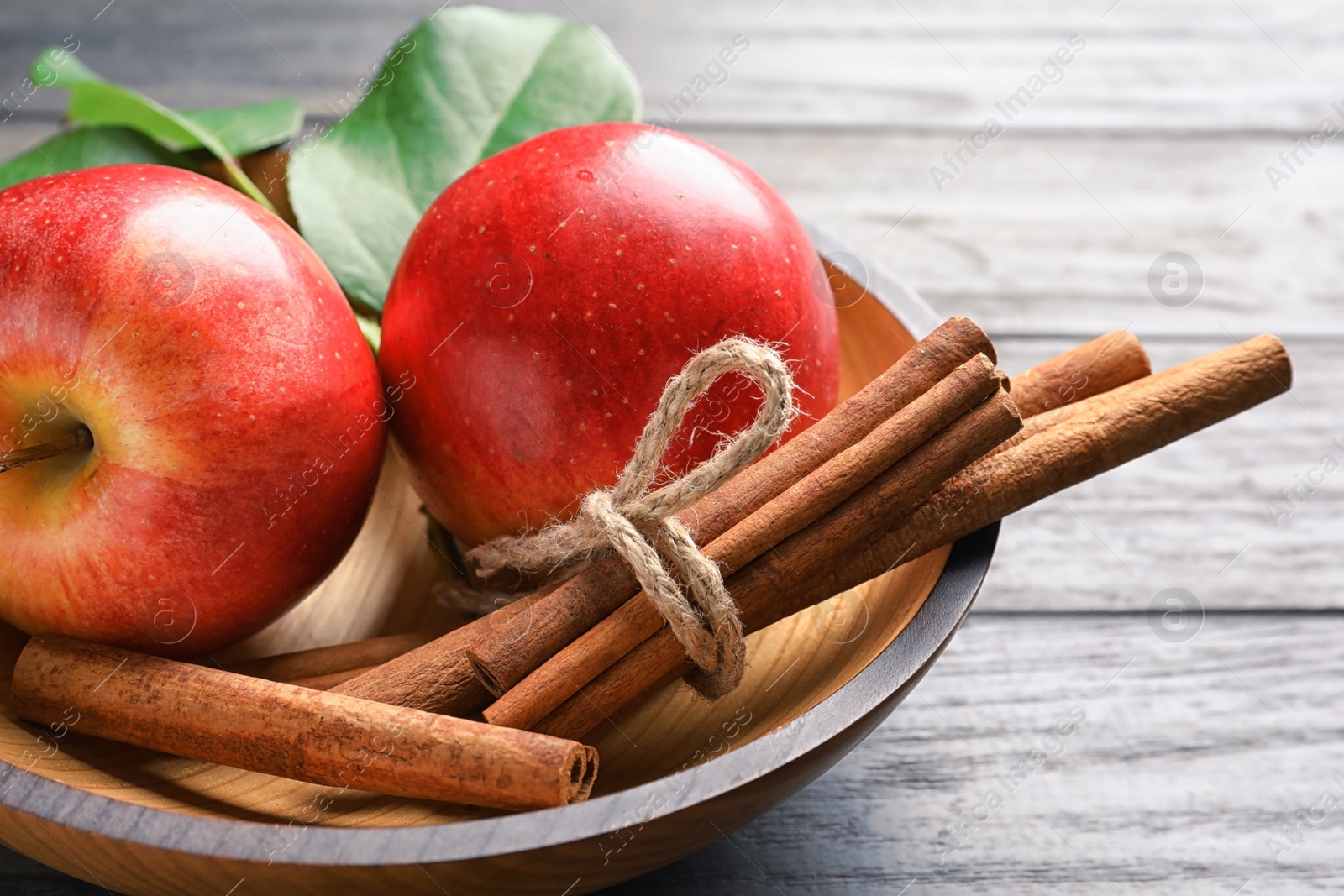 Photo of Fresh apples and cinnamon sticks in bowl, closeup