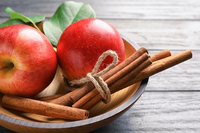 Photo of Fresh apples and cinnamon sticks in bowl, closeup