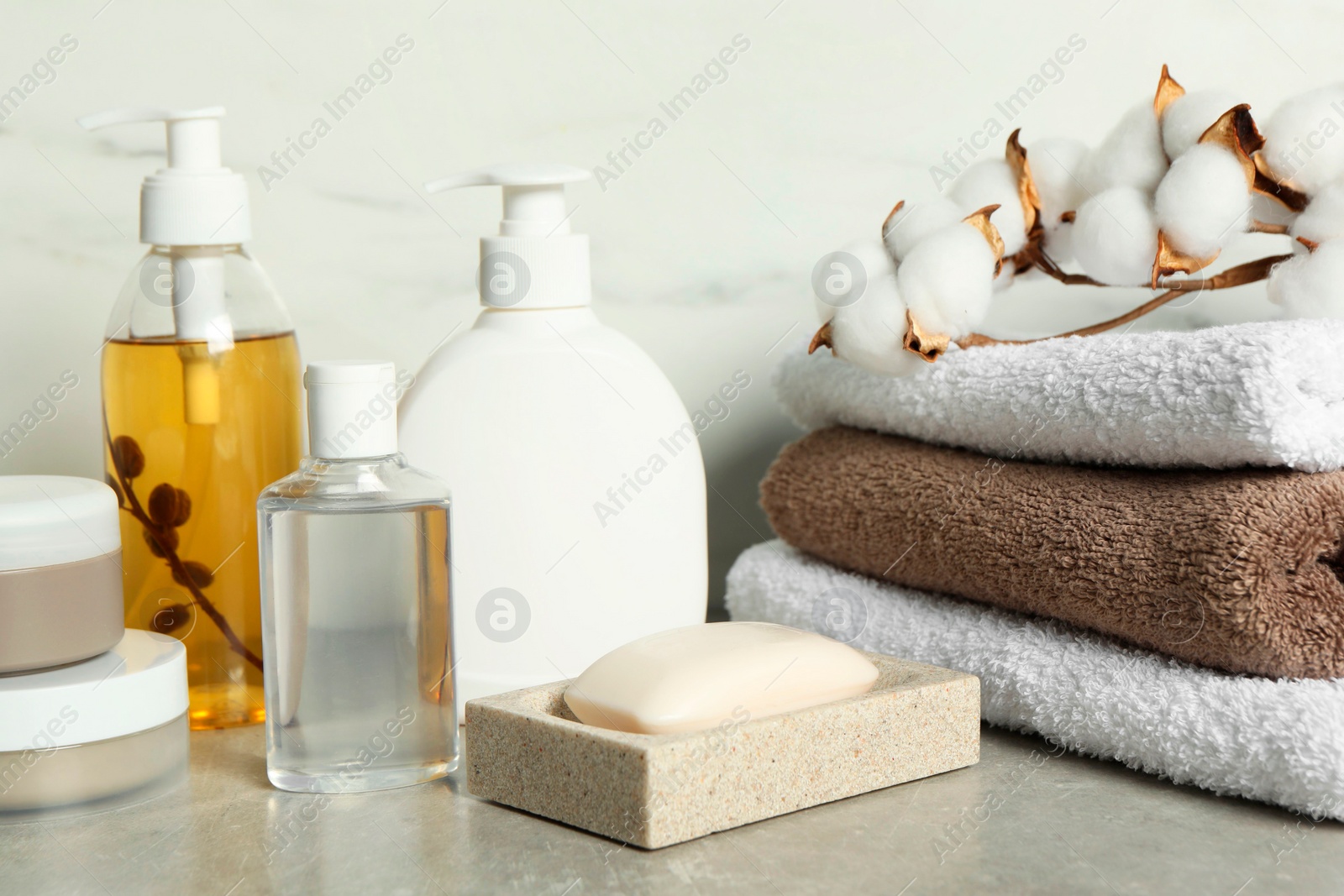 Photo of Bath accessories. Personal care products, terry towels and cotton flowers on gray table near white marble wall