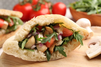 Photo of Delicious pita sandwich with cheese, mushrooms tomatoes and arugula on wooden table, closeup