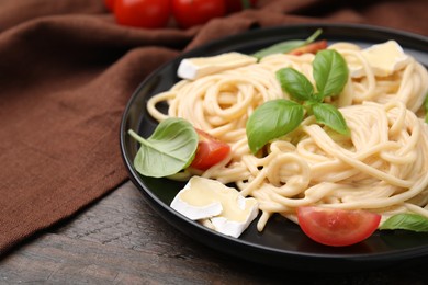 Delicious pasta with brie cheese, tomatoes and basil leaves on wooden table, closeup. Space for text