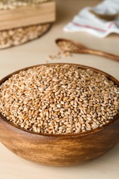 Photo of Bowl of wheat grains on white wooden table, closeup