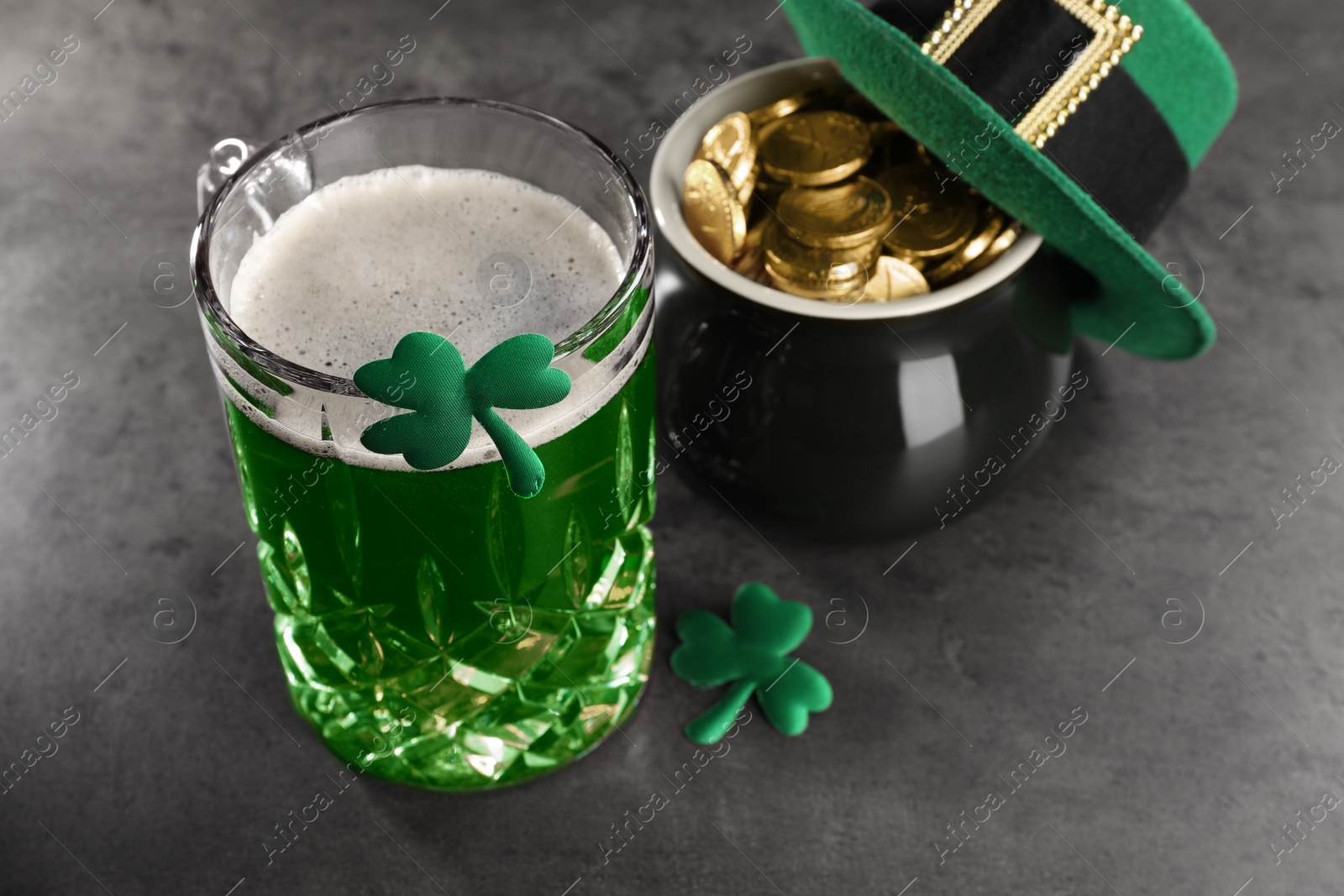 Photo of St. Patrick's day celebration. Green beer, leprechaun hat, pot of gold and decorative clover leaves on grey table