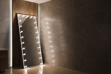 Photo of Modern mirror with light bulbs near wooden wall in room. Space for text