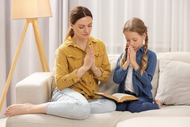 Girl and her godparent praying over Bible together on sofa at home