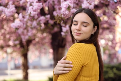 Beautiful woman near blossoming tree on spring day, space for text