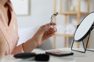 Woman with eyelash curler at dressing table indoors, closeup