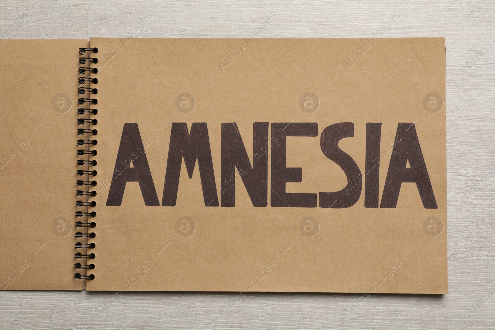 Photo of Notebook with word Amnesia on white wooden table, top view