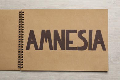Notebook with word Amnesia on white wooden table, top view