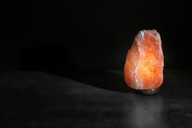 Photo of Himalayan salt lamp on table against black background. Space for text