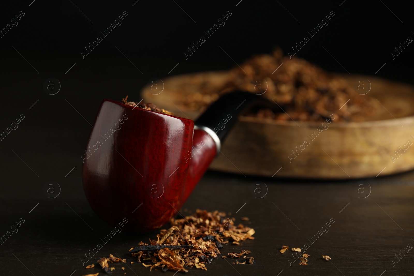 Photo of Smoking pipe and dry tobacco on dark wooden table, closeup. Space for text
