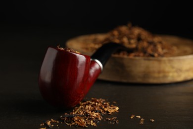 Photo of Smoking pipe and dry tobacco on dark wooden table, closeup. Space for text