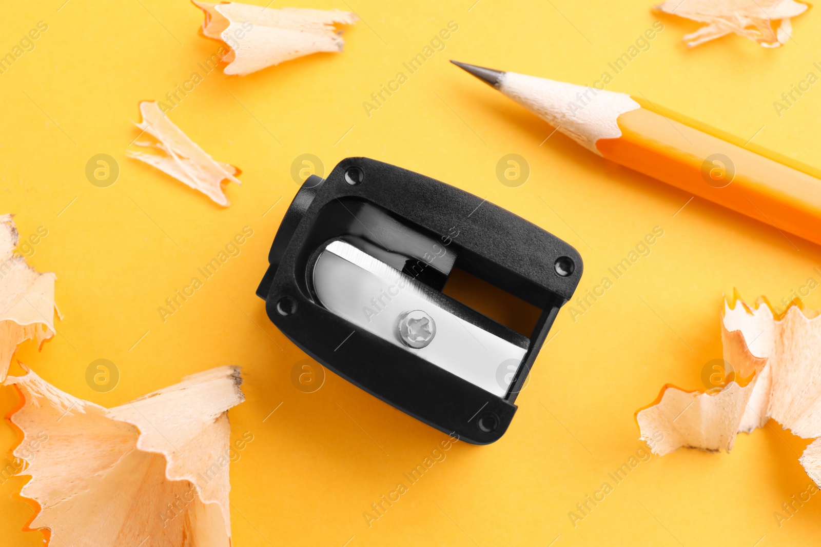 Photo of Pencil, sharpener and shavings on yellow background, flat lay