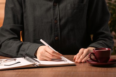 Photo of Woman writing in notebook at wooden table, closeup