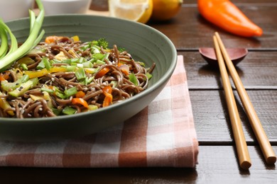 Photo of Stir-fry. Delicious cooked noodles with chicken and vegetables in bowl on wooden table, closeup