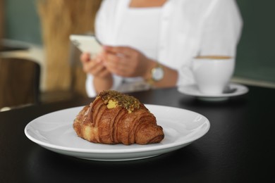 Photo of Woman sitting near tasty pastry and cup of aromatic coffee at black table in cafeteria, focus on croissant