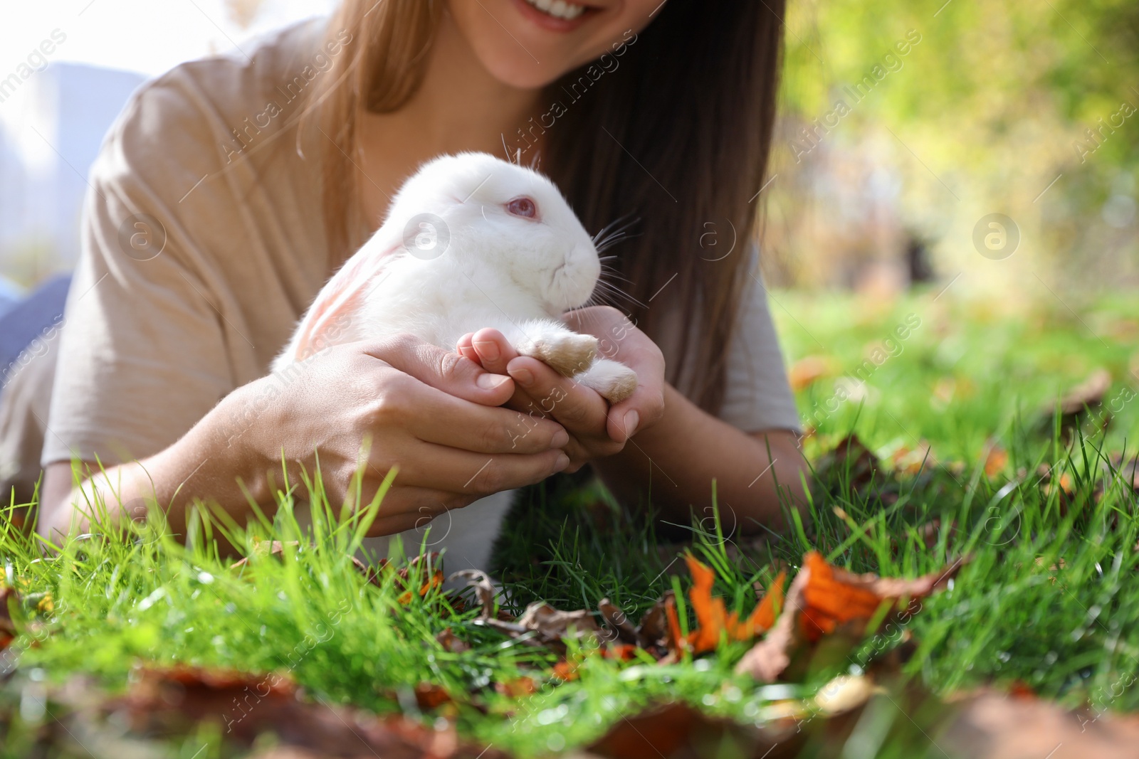 Photo of Happy woman with cute white rabbit on grass in park, closeup