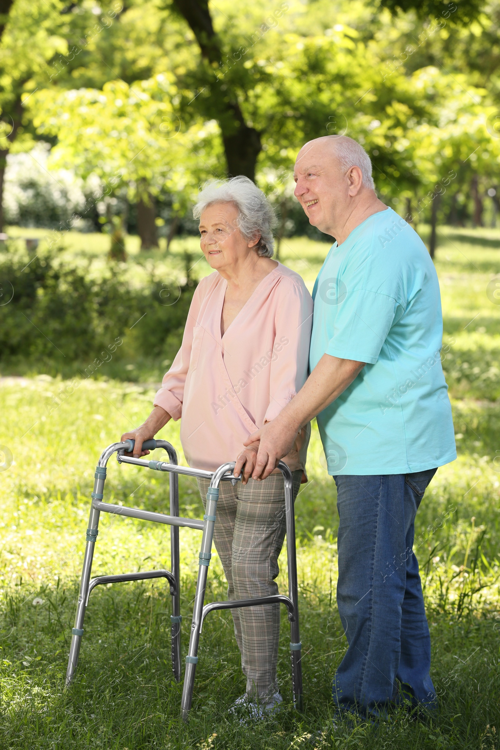 Photo of Elderly man helping his wife with walking frame outdoors