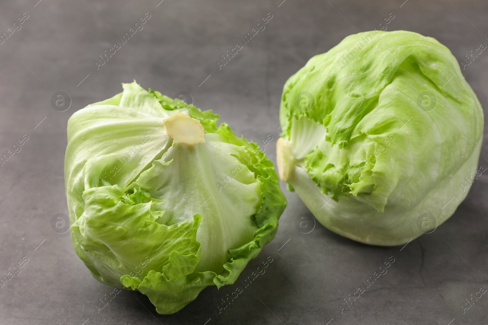 Photo of Fresh green iceberg lettuce heads on grey textured table, closeup