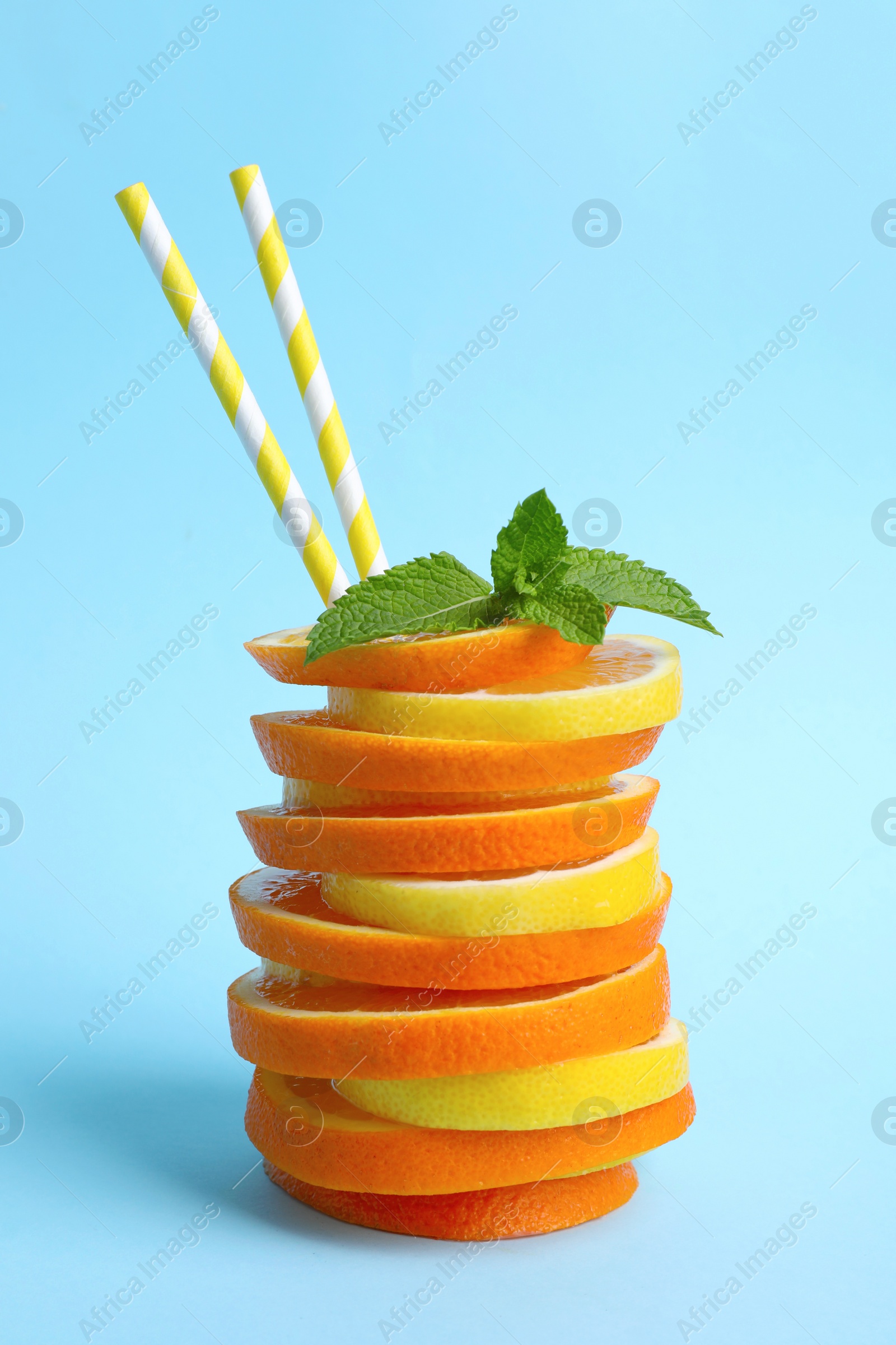 Photo of Stacked orange and lemon slices with straws as cocktail on light blue background