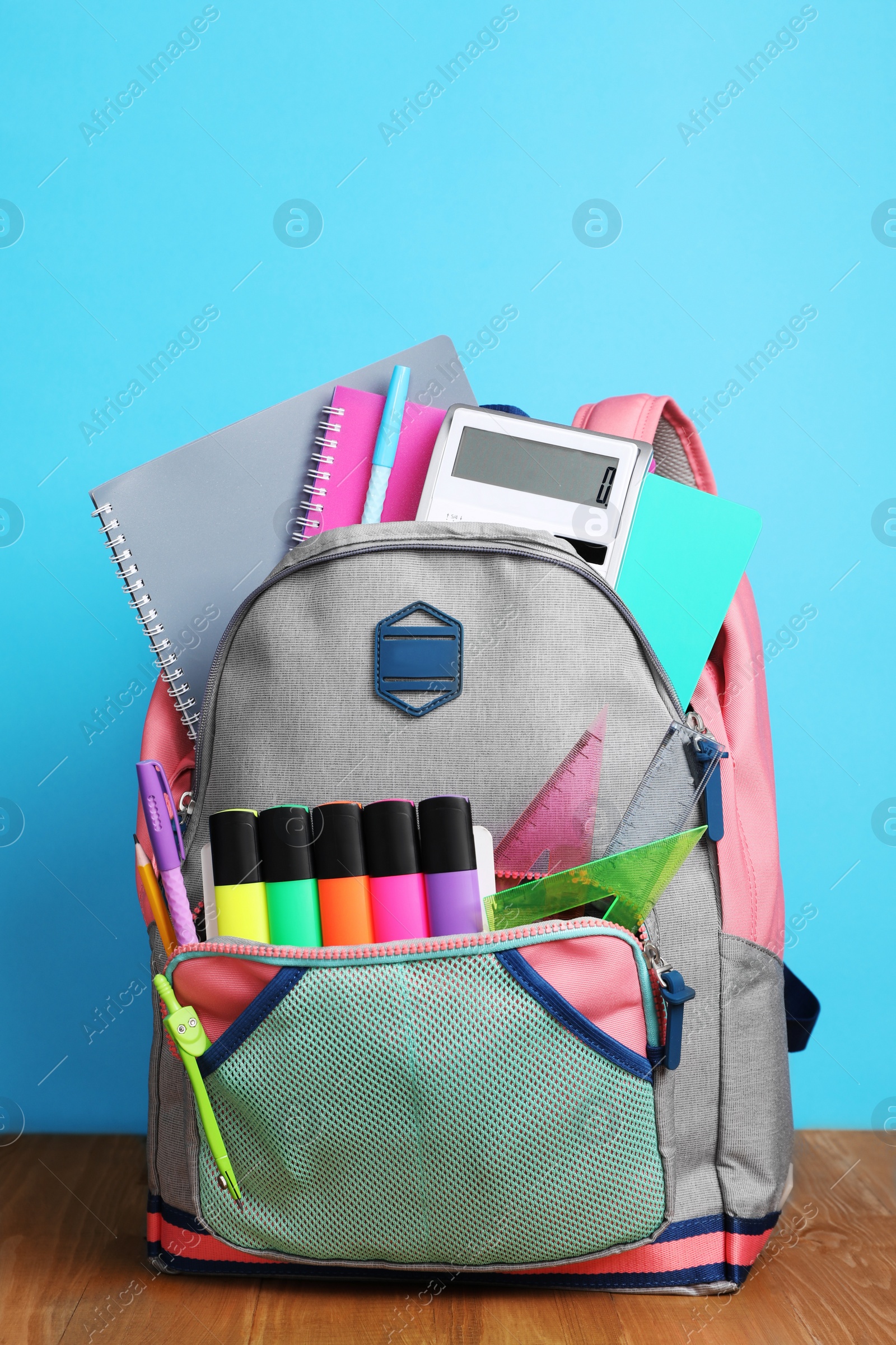 Photo of Backpack with different school stationery on wooden floor near light blue wall