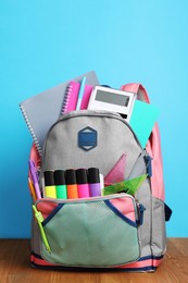 Backpack with different school stationery on wooden floor near light blue wall