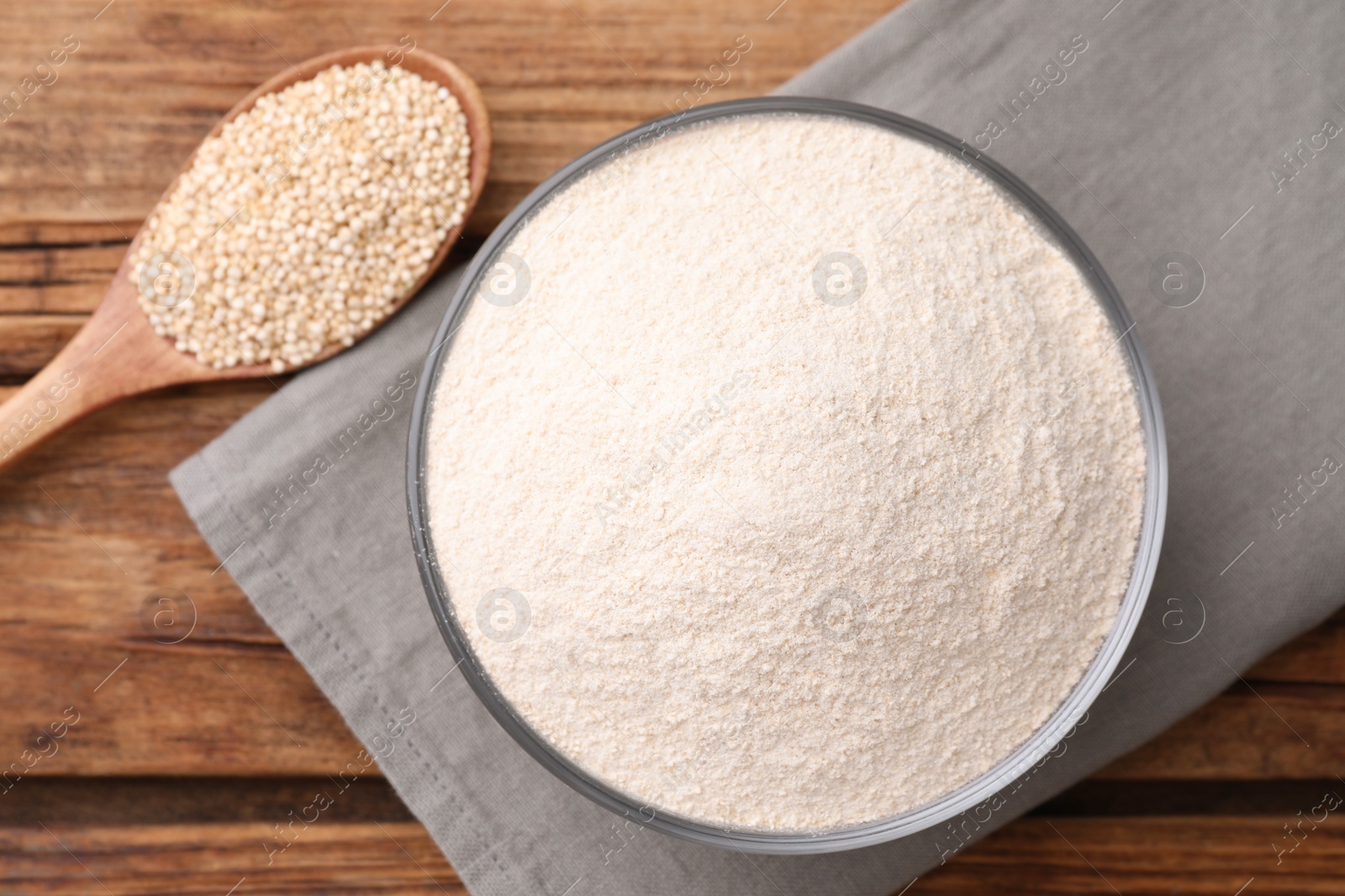 Photo of Quinoa flour in ceramic bowl and spoon with seeds on wooden table, flat lay