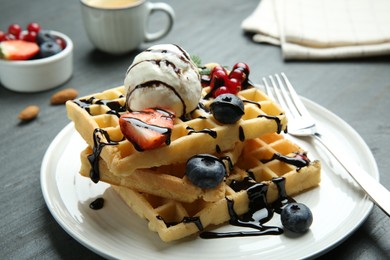 Photo of Delicious Belgian waffles with ice cream, berries and chocolate sauce served on grey textured table, closeup