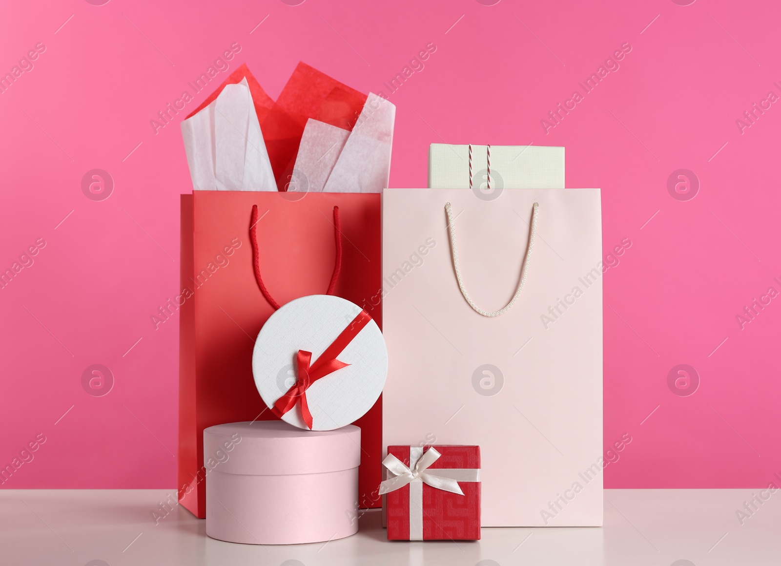 Photo of Gift bags and boxes on white table against pink background