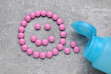 Photo of Happy emoticon made of pink antidepressants and medical jar on light grey textured background, flat lay