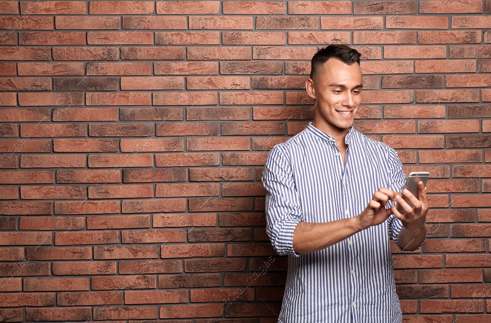 Photo of Young man with mobile phone against brick wall. Space for text