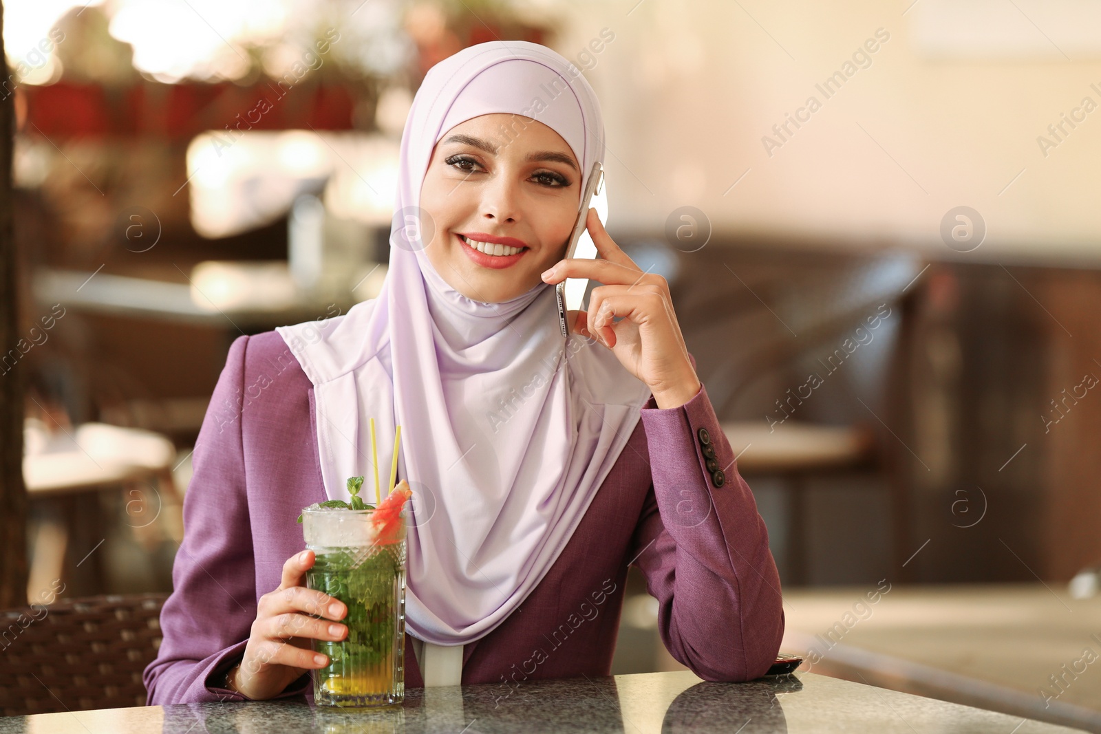 Photo of Muslim woman talking on phone in outdoor cafe