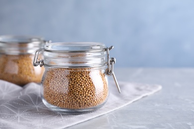 Photo of Mustard seeds in glass jar on light grey table. Space for text