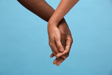 Photo of Woman and African American man holding hands on light blue background, closeup