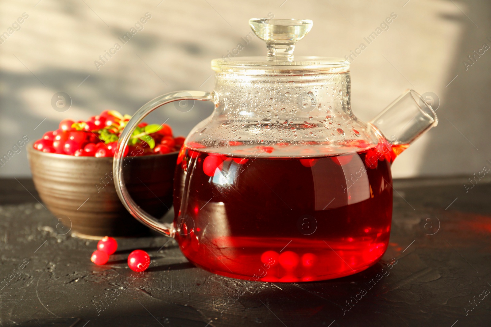 Photo of Tasty hot cranberry tea in teapot and fresh berries on black textured table