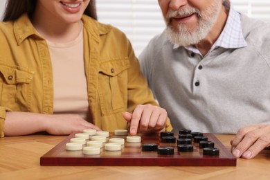 Photo of Playing checkers. Senior man learning woman at table in room, closeup