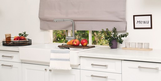 White kitchen interior with double bowl sink in front of window and fresh fruits